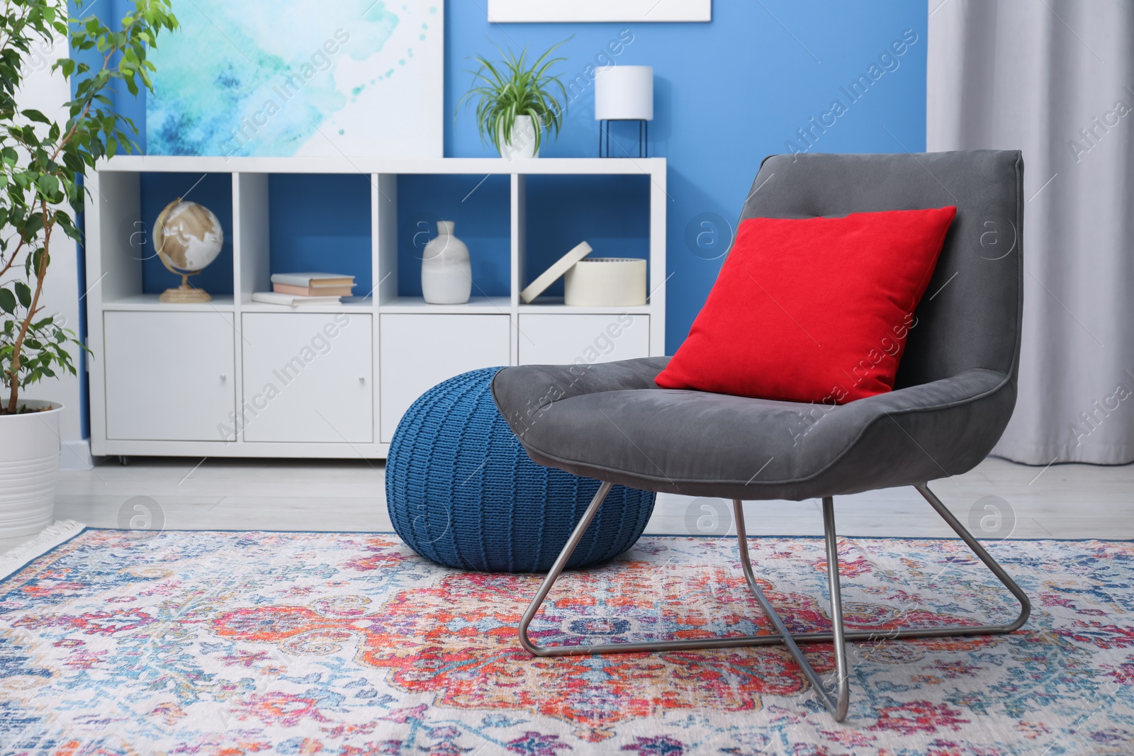 Photo of Comfortable grey armchair with red pillow in living room. Interior design