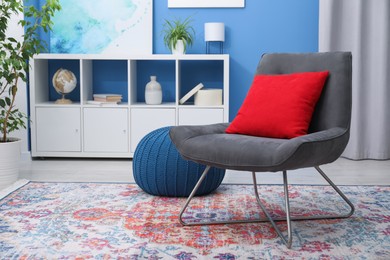 Photo of Comfortable grey armchair with red pillow in living room. Interior design