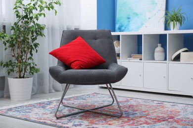 Photo of Comfortable grey armchair with red pillow in living room. Interior design