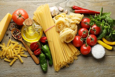 Photo of Different types of pasta and ingredients on wooden table, flat lay