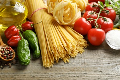 Photo of Different types of pasta and ingredients on wooden table, closeup