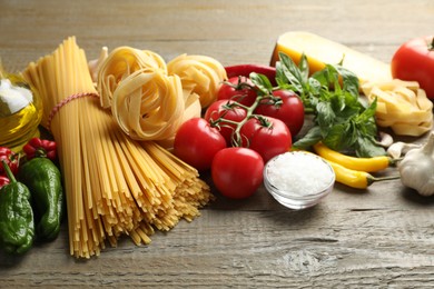 Photo of Different types of pasta and ingredients on wooden table, closeup