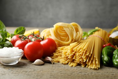 Photo of Different types of pasta and ingredients on wooden table, closeup