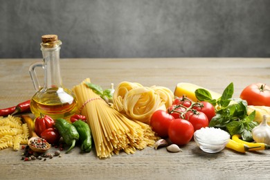 Photo of Different types of pasta and ingredients on wooden table, closeup