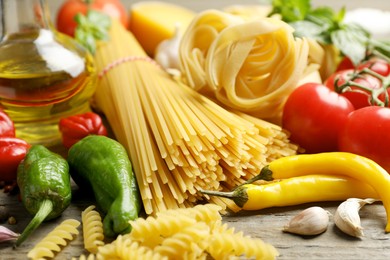 Photo of Different types of pasta and ingredients on wooden table, closeup