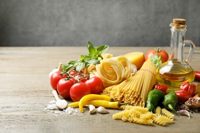 Photo of Different types of pasta and ingredients on wooden table, closeup. Space for text