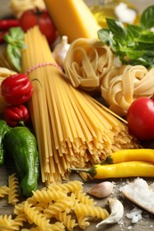 Photo of Different types of pasta and ingredients on wooden table, closeup