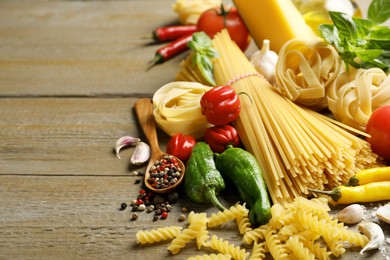 Photo of Different types of pasta and ingredients on wooden table, closeup. Space for text
