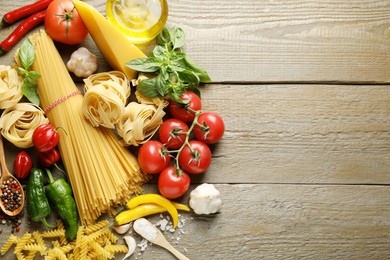 Photo of Different types of pasta and ingredients on wooden table, flat lay. Space for text