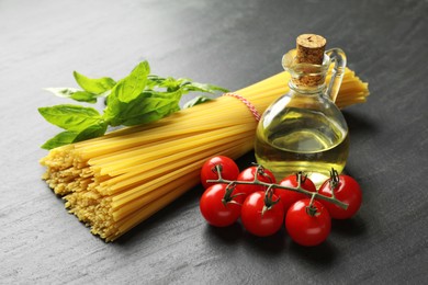 Photo of Raw spaghetti pasta and different ingredients on black table, closeup