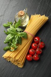 Photo of Raw spaghetti pasta and different ingredients on black table, flat lay