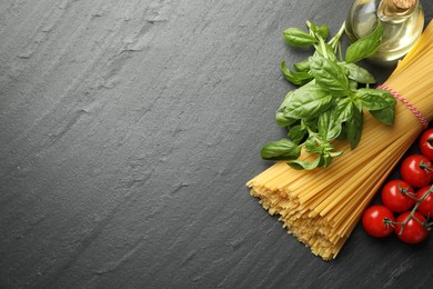 Photo of Raw spaghetti pasta and different ingredients on black table, flat lay. Space for text