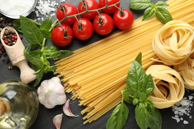 Photo of Different types of pasta and ingredients on black table, flat lay