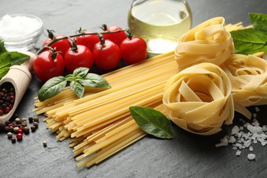 Photo of Different types of pasta and ingredients on black table, closeup