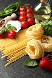 Photo of Different types of pasta and ingredients on black table, closeup
