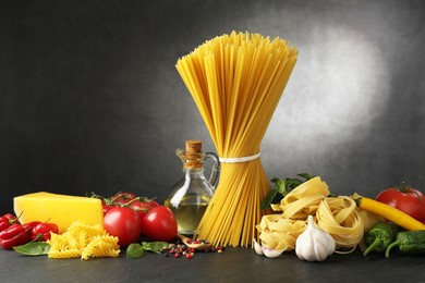Photo of Different types of pasta and ingredients on black table