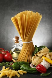 Photo of Different types of pasta and ingredients on black table, closeup