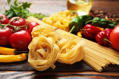 Photo of Different types of pasta and ingredients on wooden table, closeup