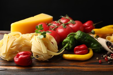 Photo of Raw tagliatelle pasta and different ingredients on wooden table, closeup