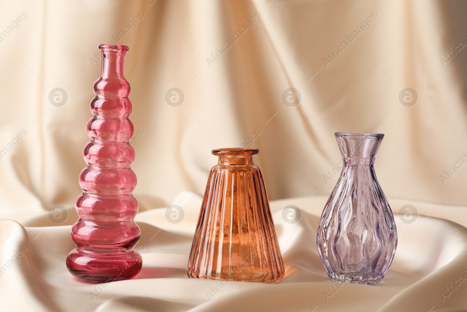 Photo of Different beautiful glass vases on beige cloth