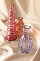 Photo of Different beautiful glass vases on beige cloth, closeup