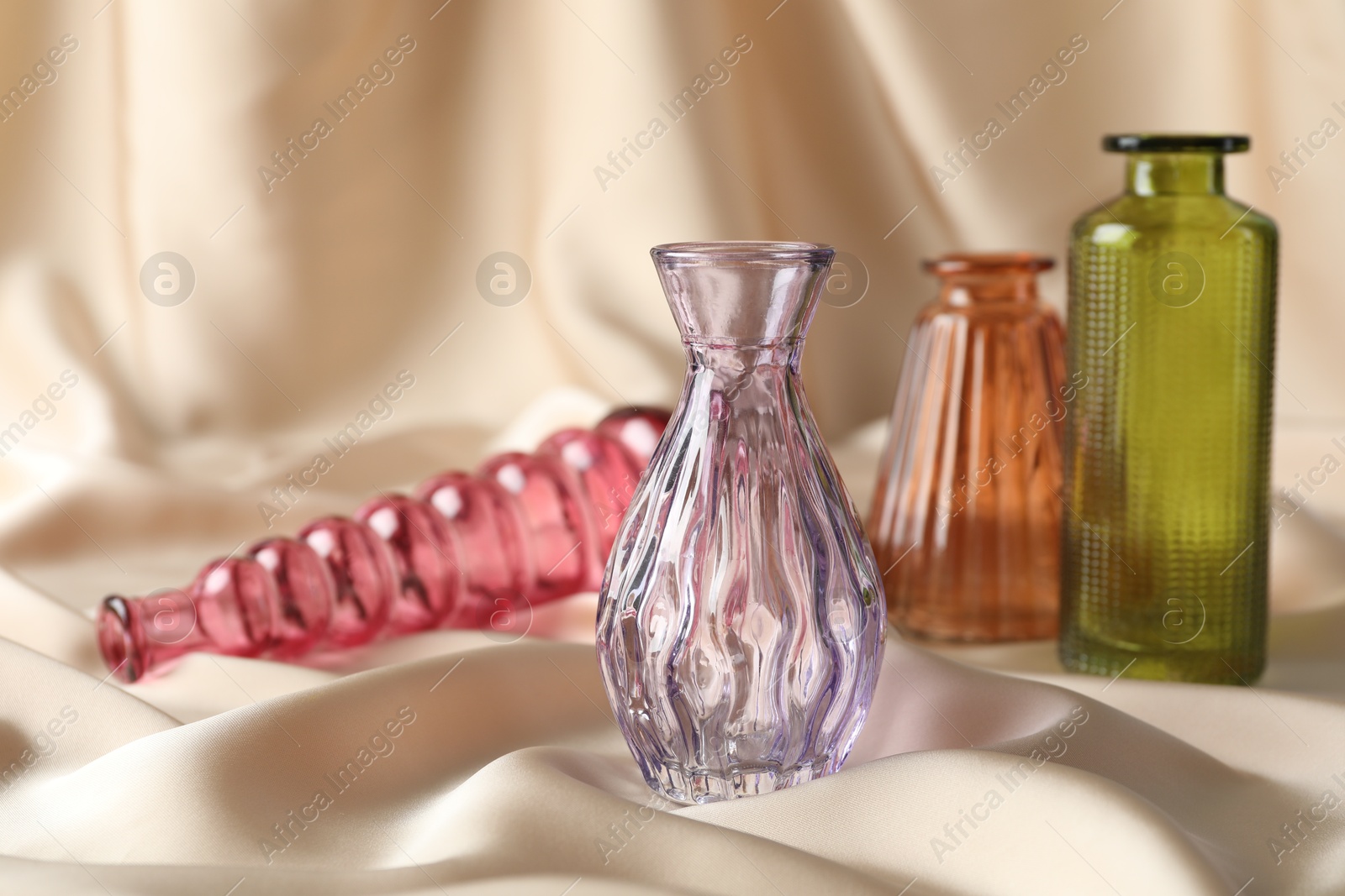 Different beautiful glass vases on beige cloth, space for text Photo of Different beautiful glass vases on beige cloth, space for text