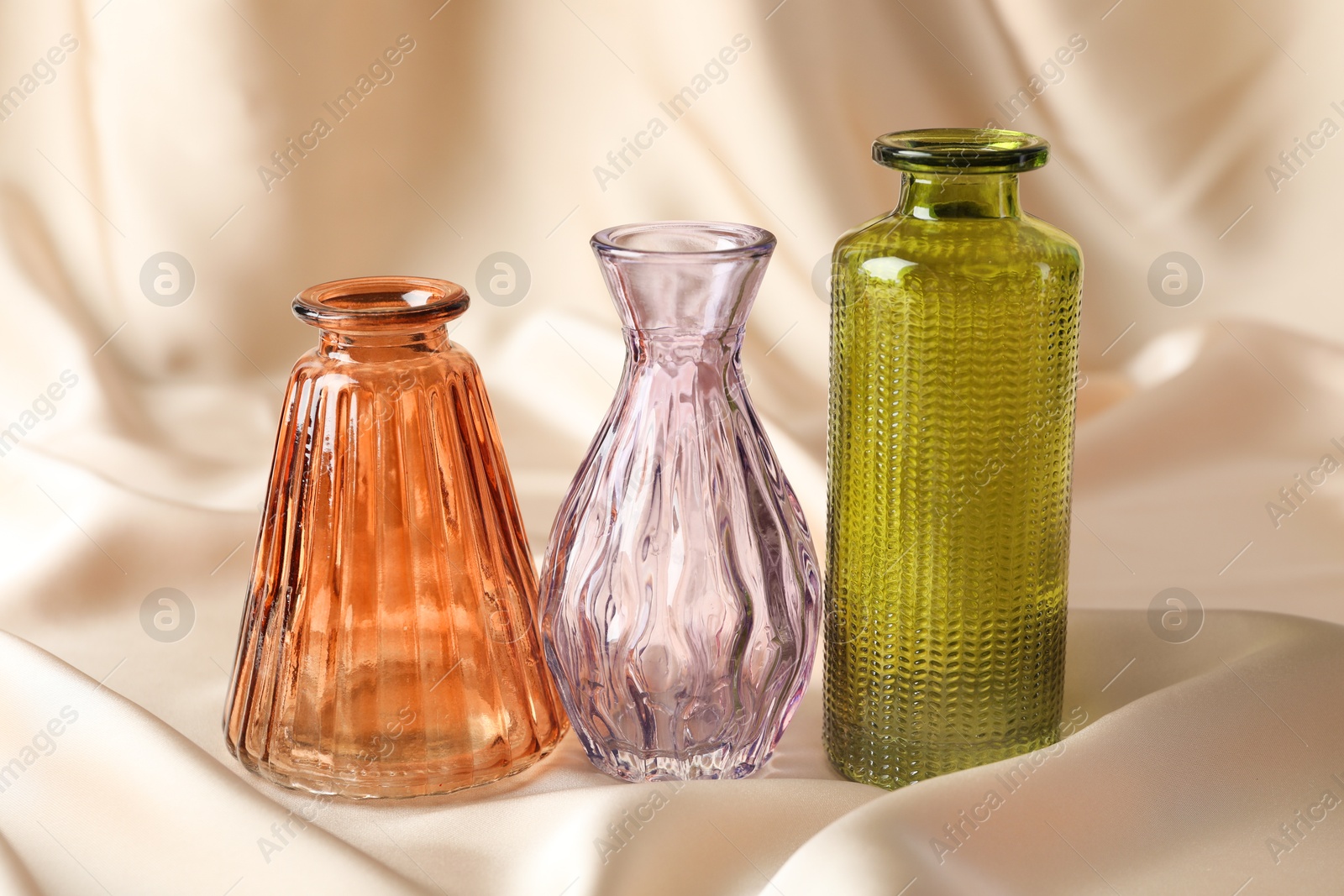 Photo of Different beautiful glass vases on beige cloth