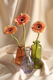 Photo of Beautiful flowers in glass vases on beige cloth, closeup