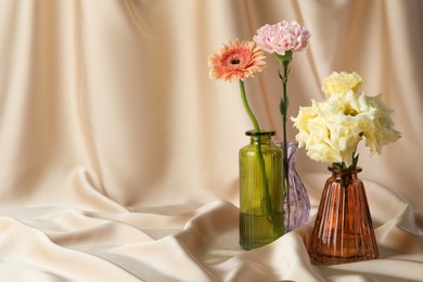 Photo of Beautiful flowers in glass vases on beige cloth, space for text