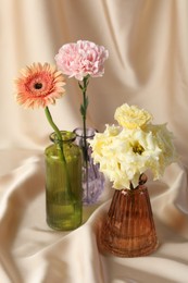 Photo of Beautiful flowers in glass vases on beige cloth, closeup