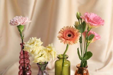 Photo of Beautiful flowers in glass vases against beige cloth, closeup