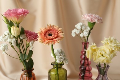 Photo of Beautiful flowers in glass vases against beige cloth, closeup