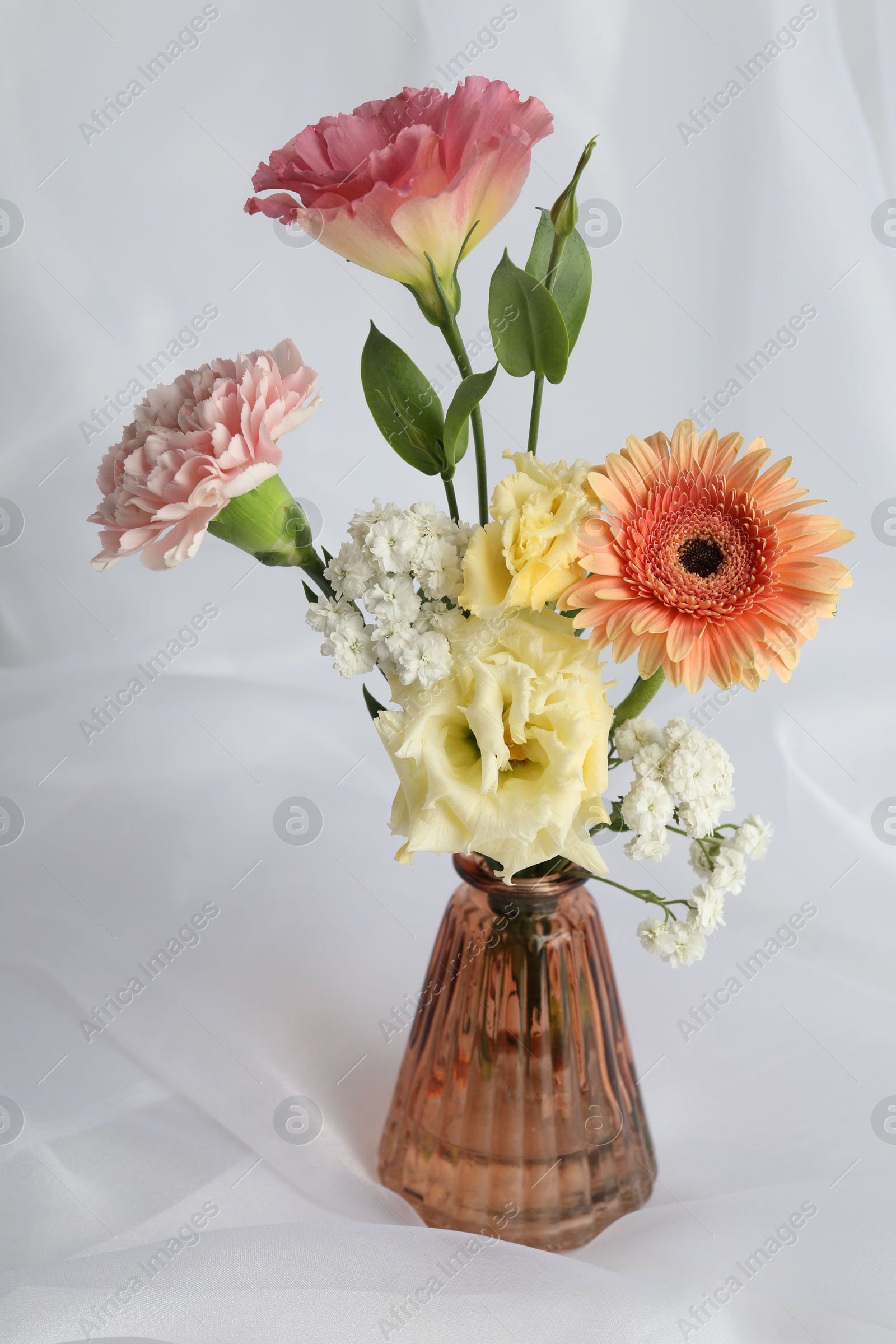 Photo of Beautiful flowers in glass vase on white cloth, closeup