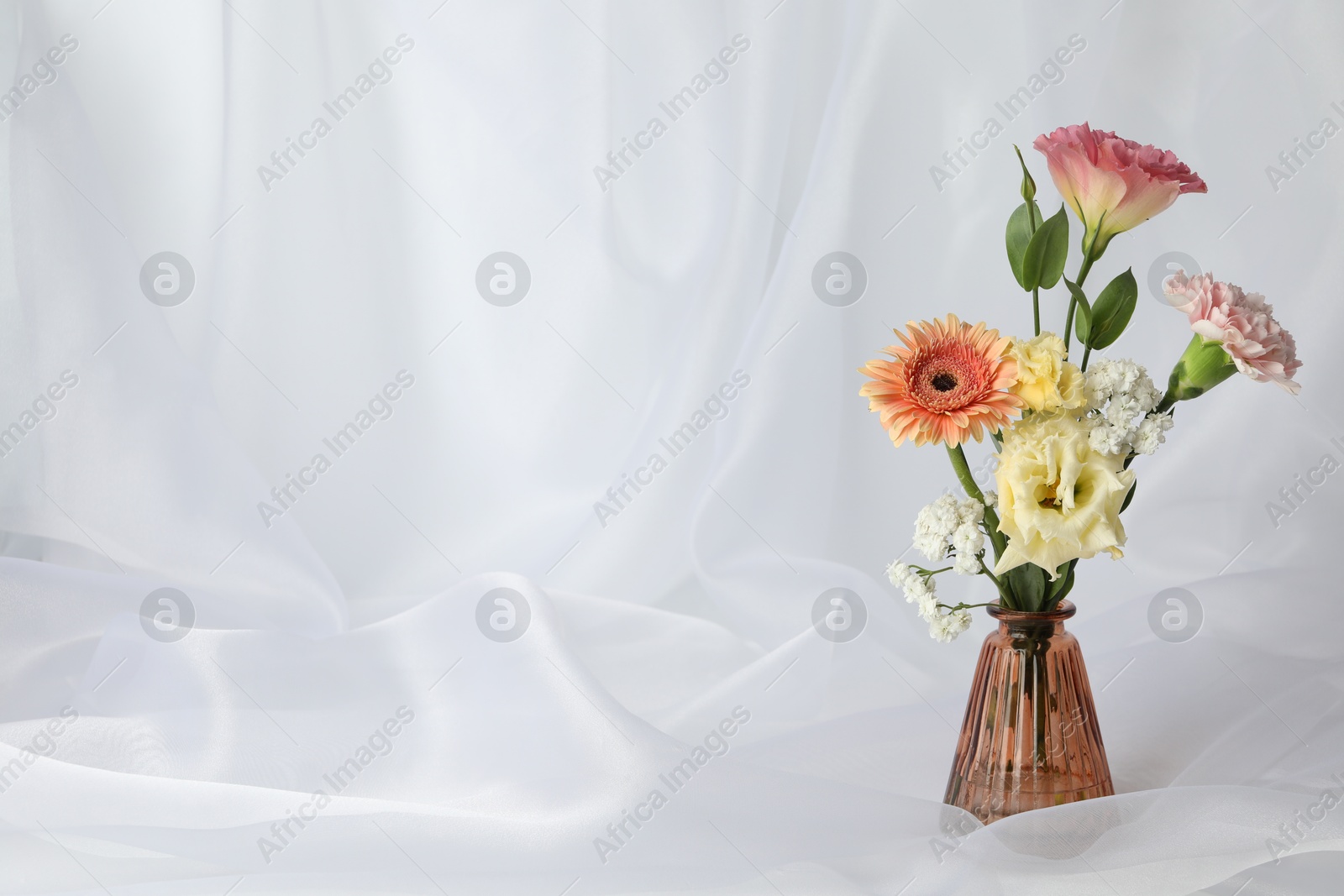 Beautiful flowers in glass vase on white cloth, space for text Photo of Beautiful flowers in glass vase on white cloth, space for text