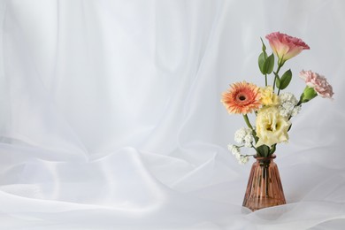 Photo of Beautiful flowers in glass vase on white cloth, space for text