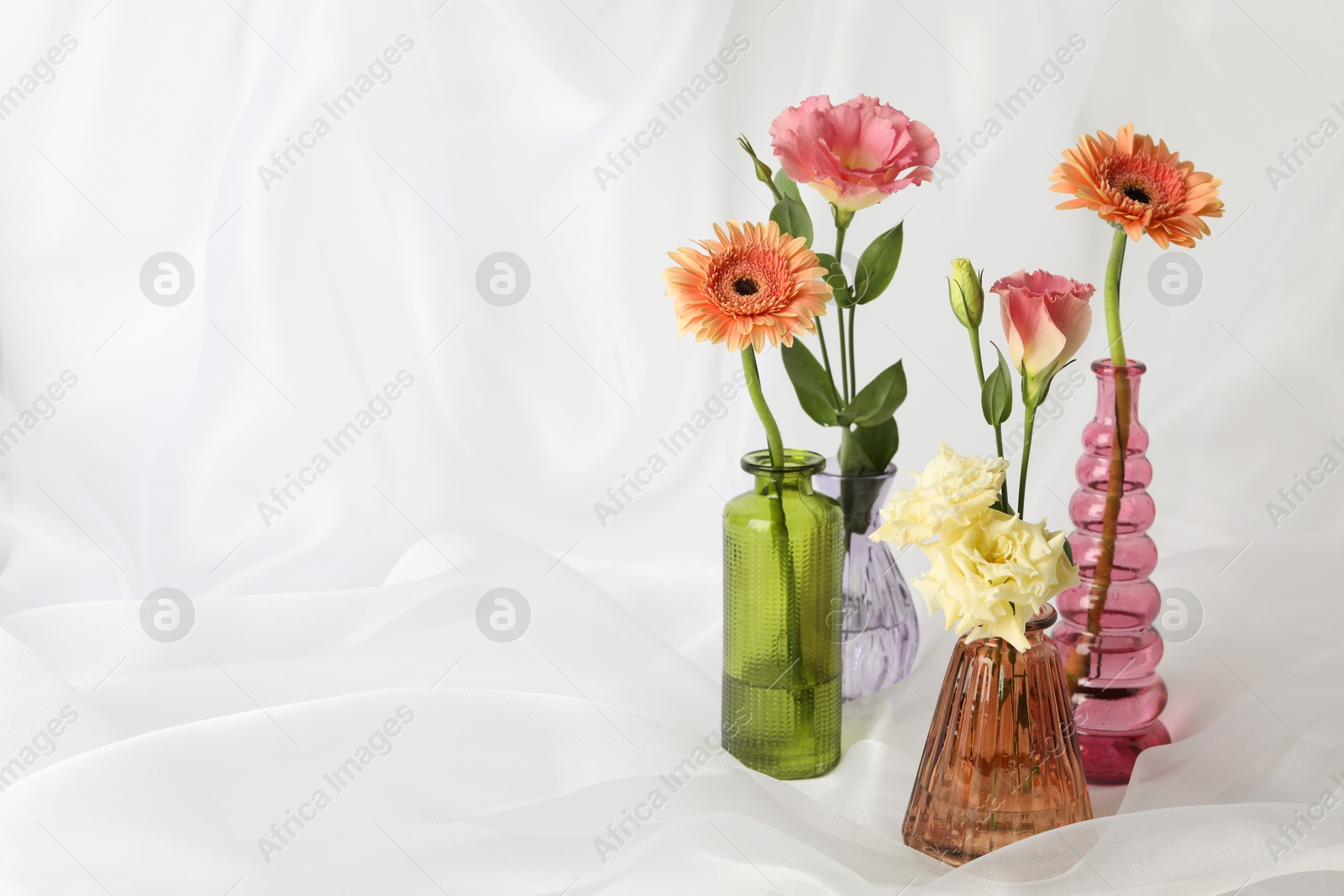 Beautiful flowers in glass vases on white cloth, space for text Photo of Beautiful flowers in glass vases on white cloth, space for text