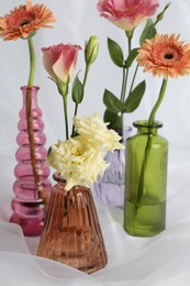 Photo of Beautiful flowers in glass vases on white cloth, closeup