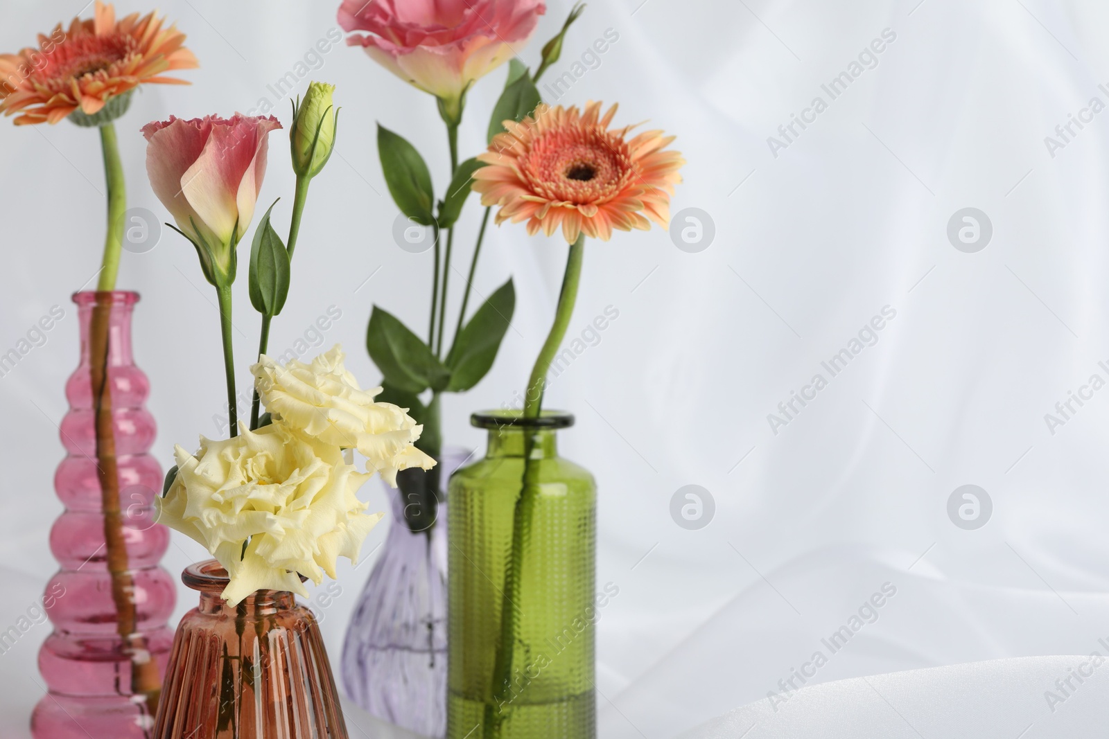 Beautiful flowers in glass vases on white cloth, closeup. Space for text Photo of Beautiful flowers in glass vases on white cloth, closeup. Space for text