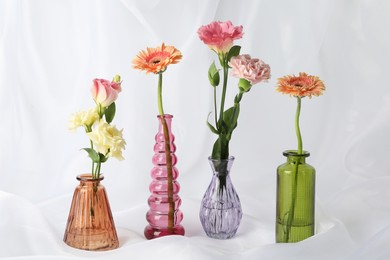 Photo of Beautiful flowers in glass vases on white cloth