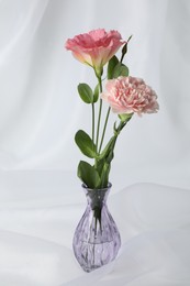 Photo of Beautiful flowers in glass vase on white cloth, closeup