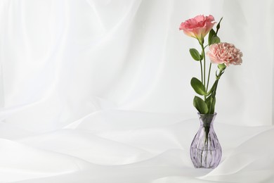 Photo of Beautiful flowers in glass vase on white cloth, space for text