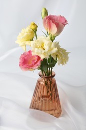 Photo of Beautiful flowers in glass vase on white cloth, closeup