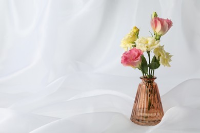 Photo of Beautiful flowers in glass vase on white cloth, space for text