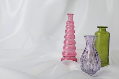 Photo of Different beautiful glass vases on white cloth, closeup. Space for text