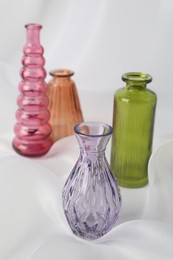 Photo of Different beautiful glass vases on white cloth, closeup