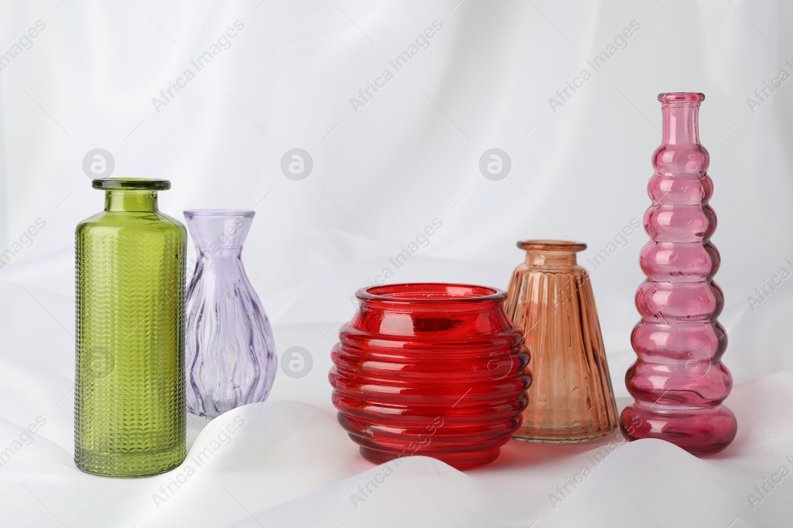 Different beautiful glass vases on white cloth Photo of Different beautiful glass vases on white cloth