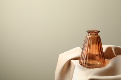 Photo of One beautiful glass vase on beige cloth against light background, space for text