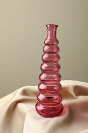 Photo of One beautiful glass vase on beige cloth against light background, closeup