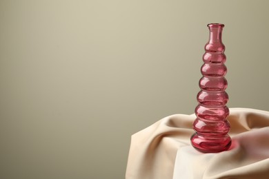 Photo of One beautiful glass vase on beige cloth against light background, space for text