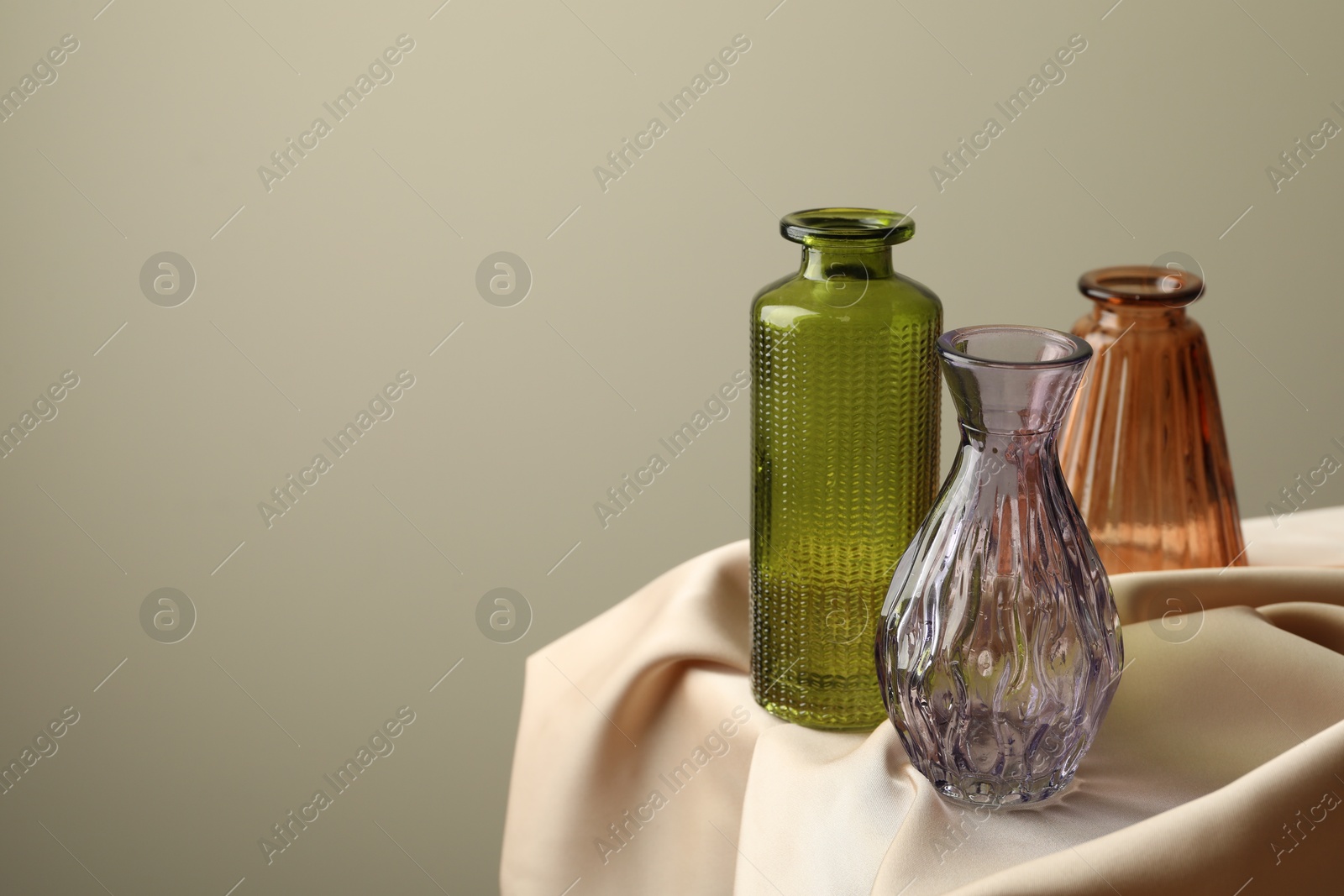 Different beautiful glass vases on beige cloth against light background, closeup. Space for text Photo of Different beautiful glass vases on beige cloth against light background, closeup. Space for text